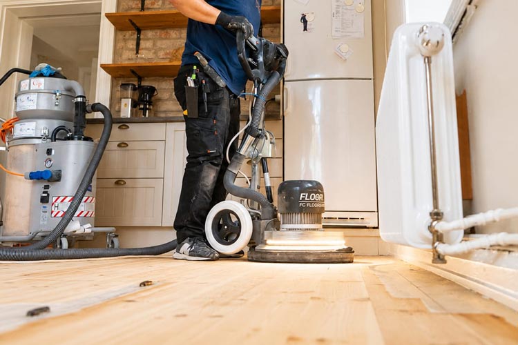Medarbetare som slipar trägolv med professionell golvslipningsmaskin